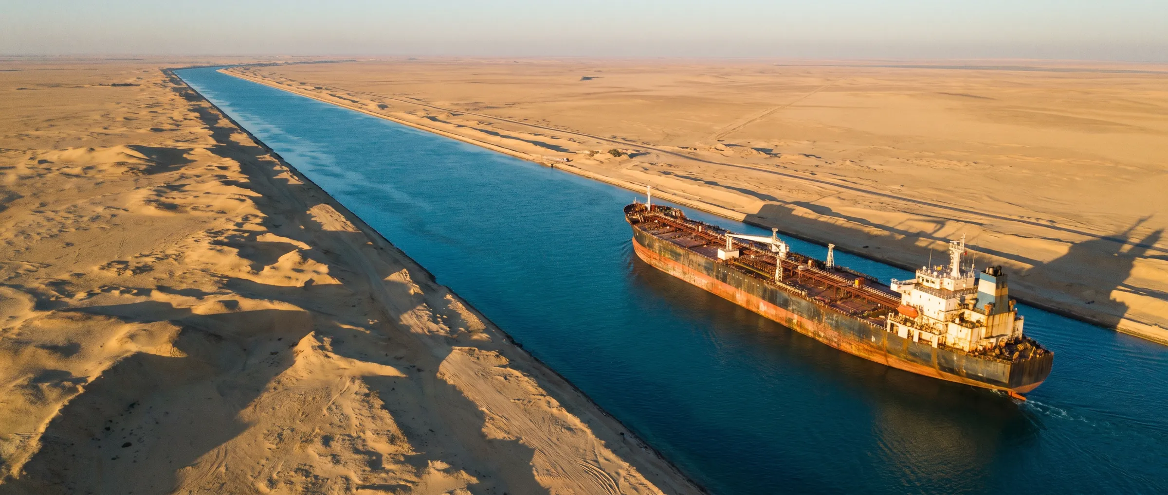 A tanker transiting a canal through the desert at sunrise