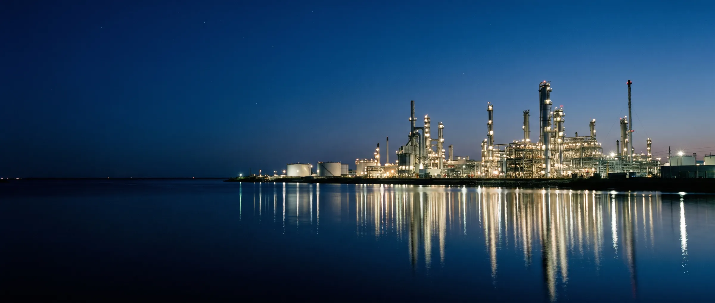 An oil refinery lit at blue hour and reflected in calm water